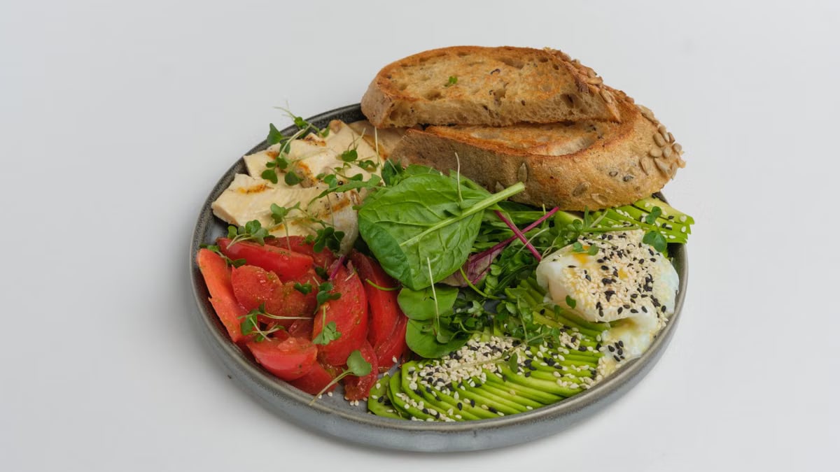 Delicious breakfast plate with toast, avocado, poached egg, and fresh vegetables.
